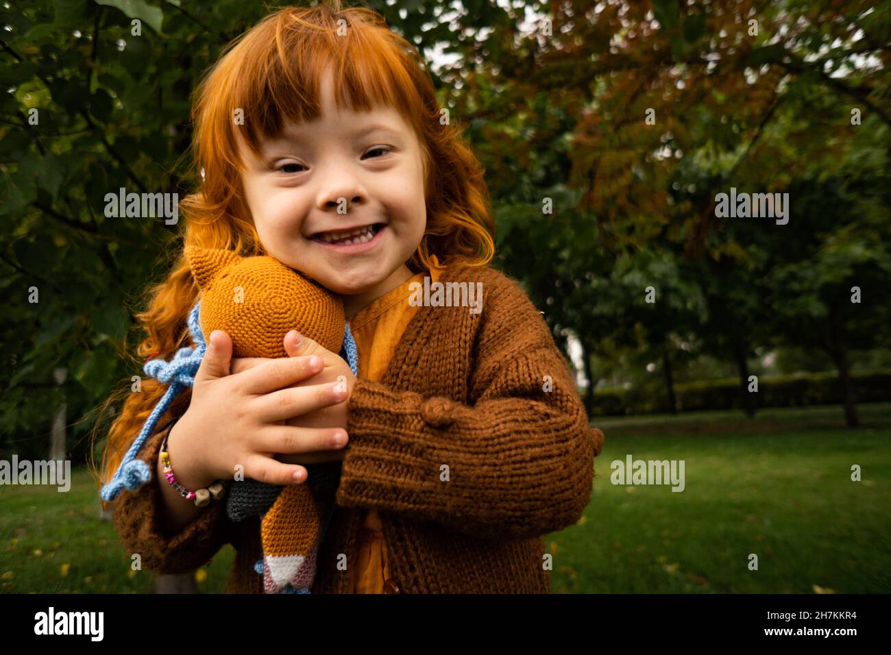Lächelndes Mädchen mit Down-Syndrom umarmen Spielzeug im Park Stockfoto
