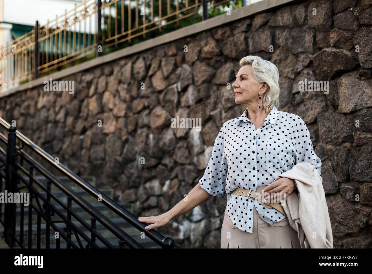 Ältere Frau, die vor einer Steinmauer steht Stockfoto