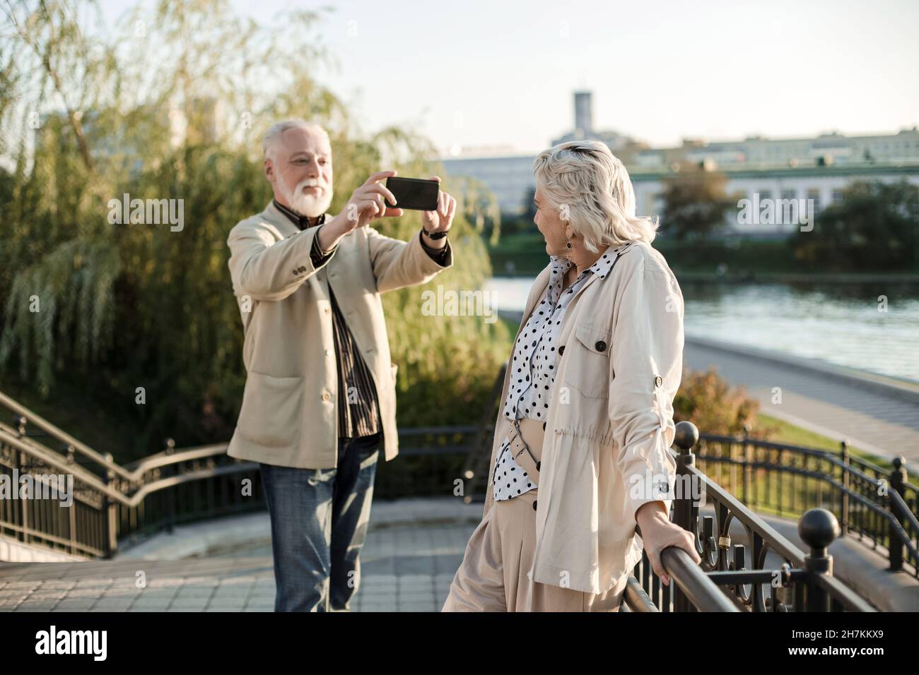 Mann, der eine Frau über ein Smartphone fotografiert, während er auf der Brücke steht Stockfoto