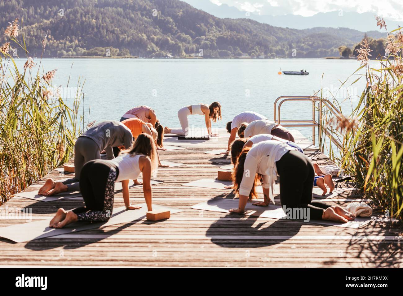 Weibliche Lehrerin, die Frauen und Männern am Steg am See Yoga beibringt Stockfoto