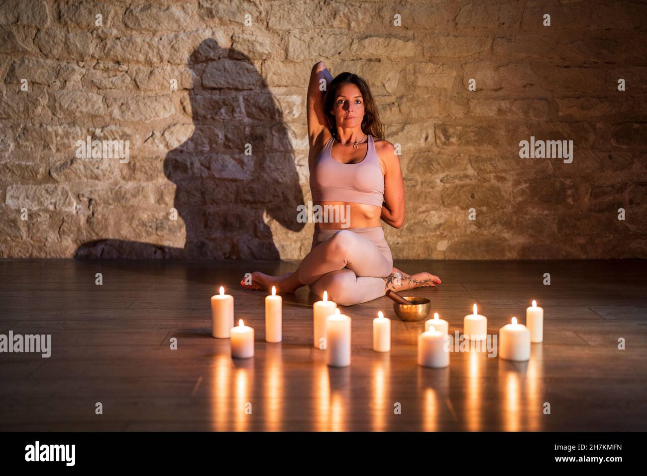 Frau übt Gomukhasana an Kerzen auf dem Boden Stockfoto