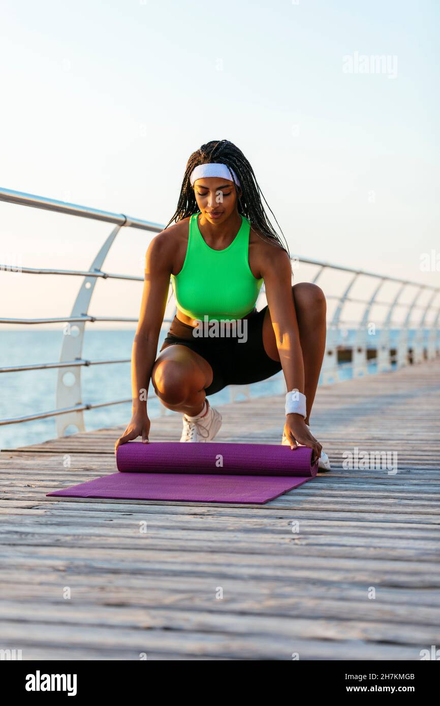 Junge Sportlerin legt Yogamatte auf Broadwalk Stockfoto