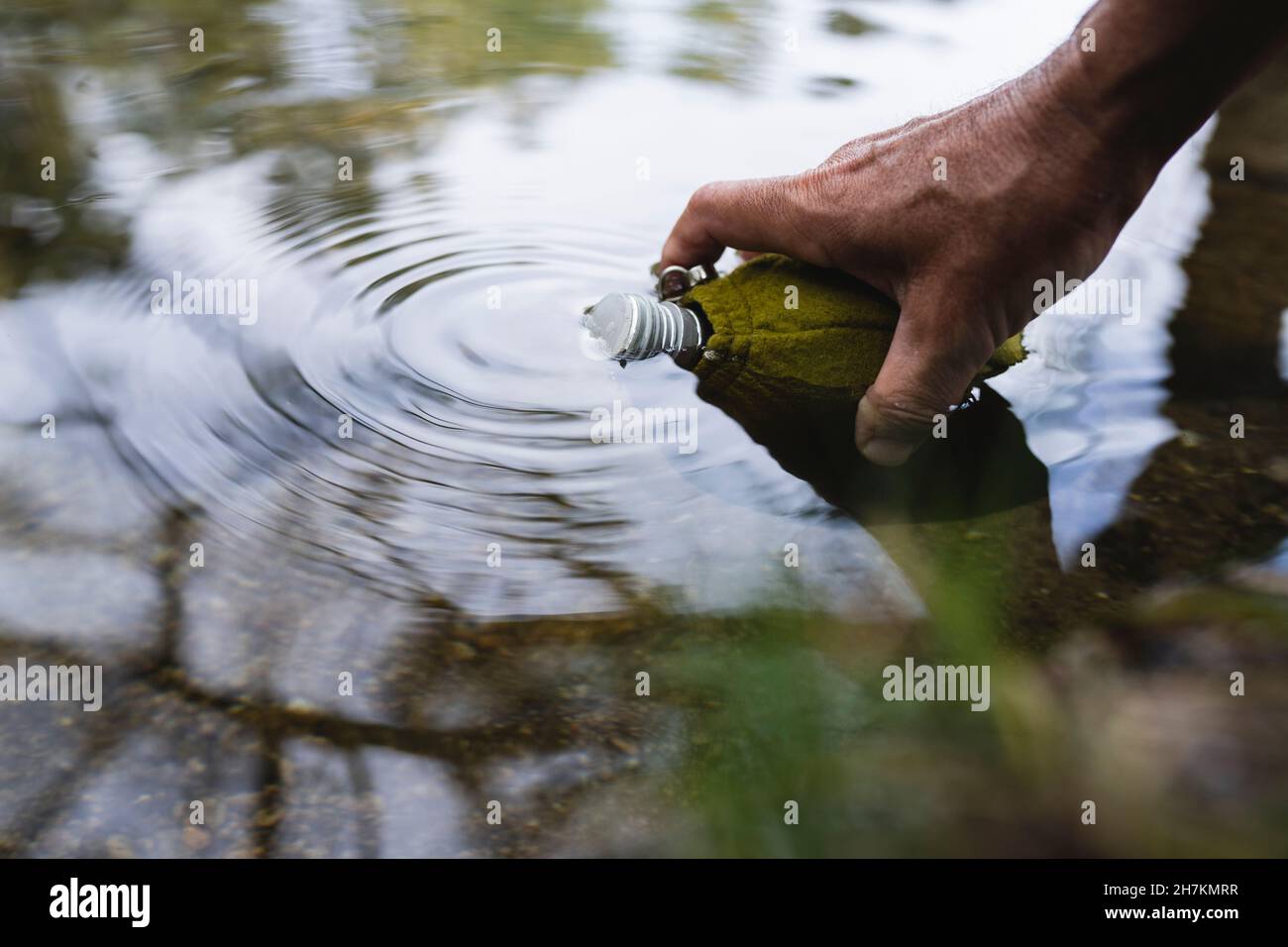 Reifer Mann, der während des Urlaubs Wasser in die Flasche am Teich füllte Stockfoto