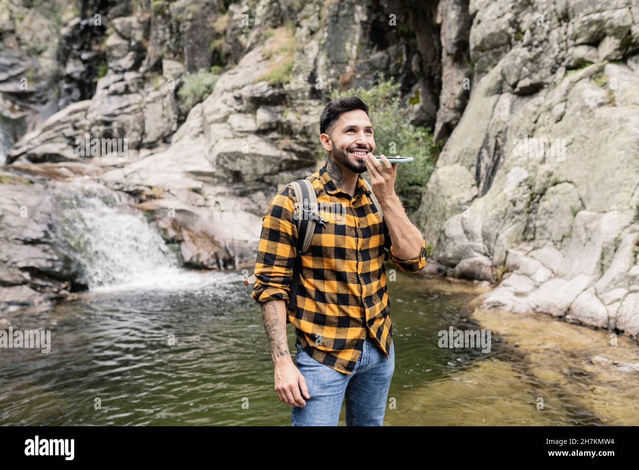 Lächelnder Mann mit mittlerem Erwachsenen, der Rucksack trägt und am Teich im Wald steht Stockfoto