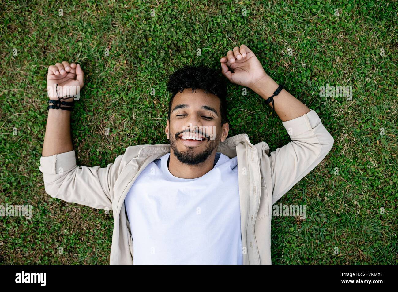 Glücklicher junger Mann mit geschlossenen Augen, der sich auf dem Gras entspannt Stockfoto