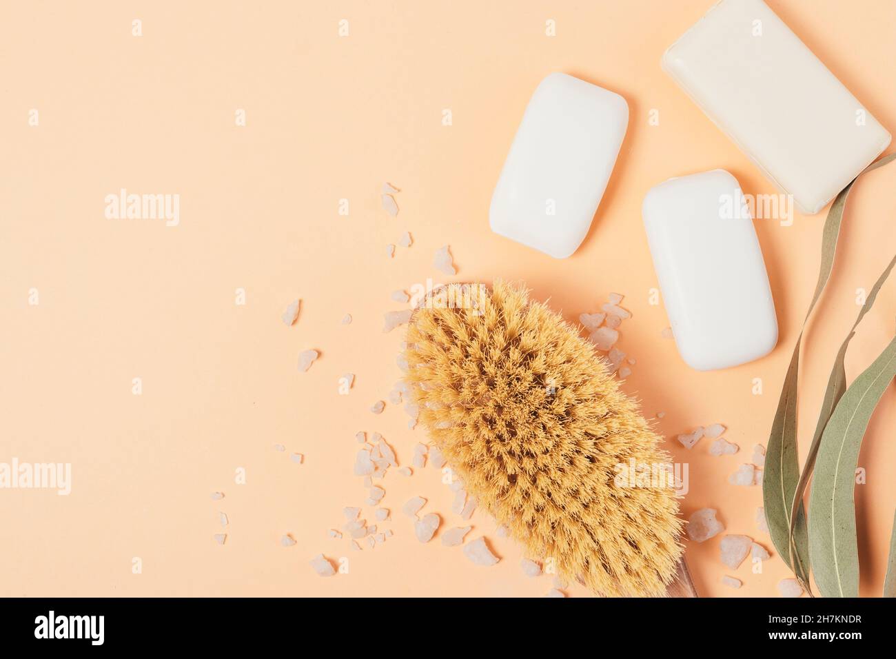 Massagebürste mit Seifenstücken und Badesalz auf pfirsichfarbenem Hintergrund Stockfoto