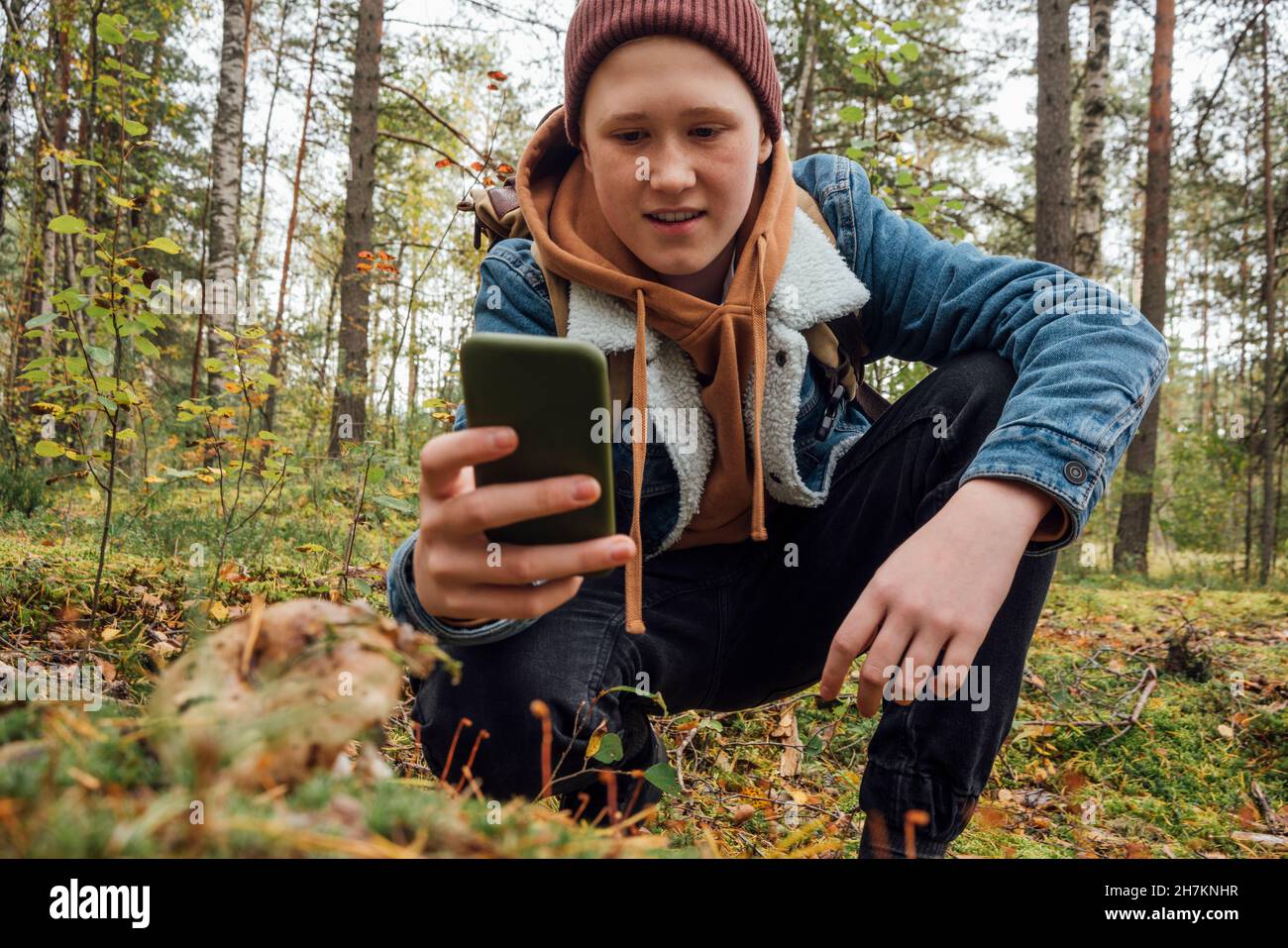 Junge fotografiert durch Smartphone, während er im Wald kniet Stockfoto