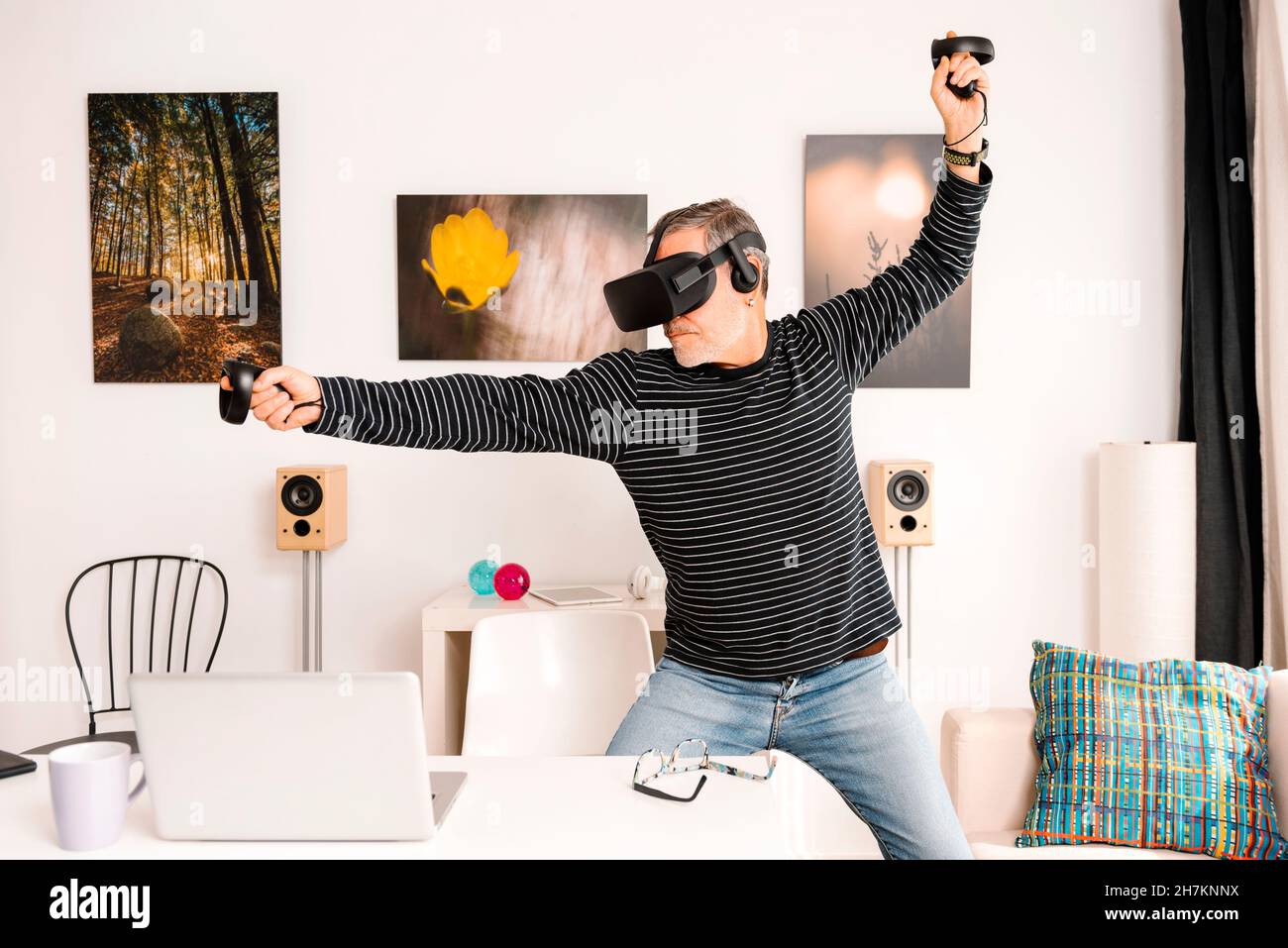 Fröhlicher Mann mit Virtual-Reality-Simulator zeigt beim Stehen am Tisch Stockfoto