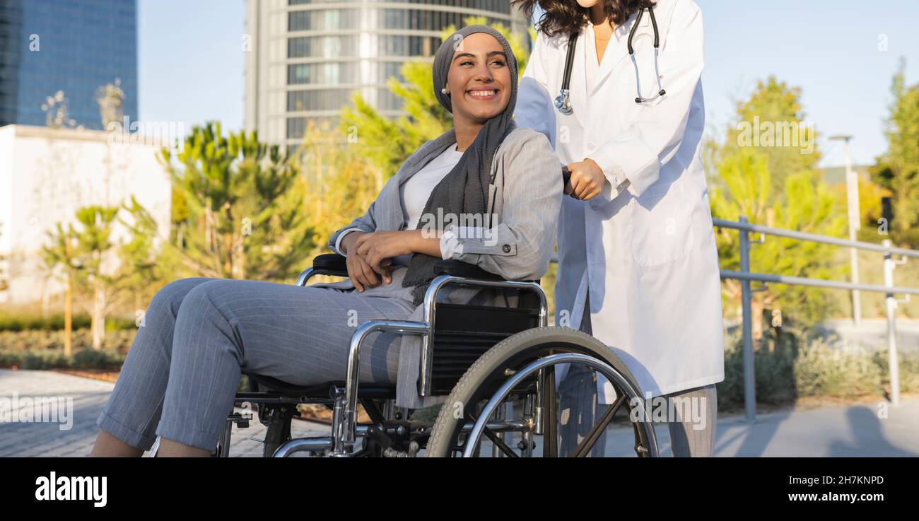 Behinderte Frau, die die Hand einer medizinischen Mitarbeiterin in der Hand hält, während sie im Rollstuhl sitzt Stockfoto