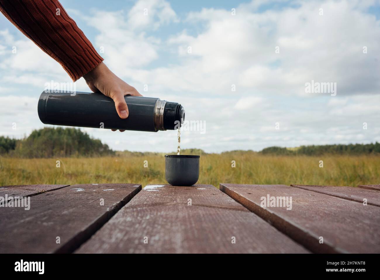 Mann gießt Tee aus isolierter Flasche in die Tasse Stockfoto