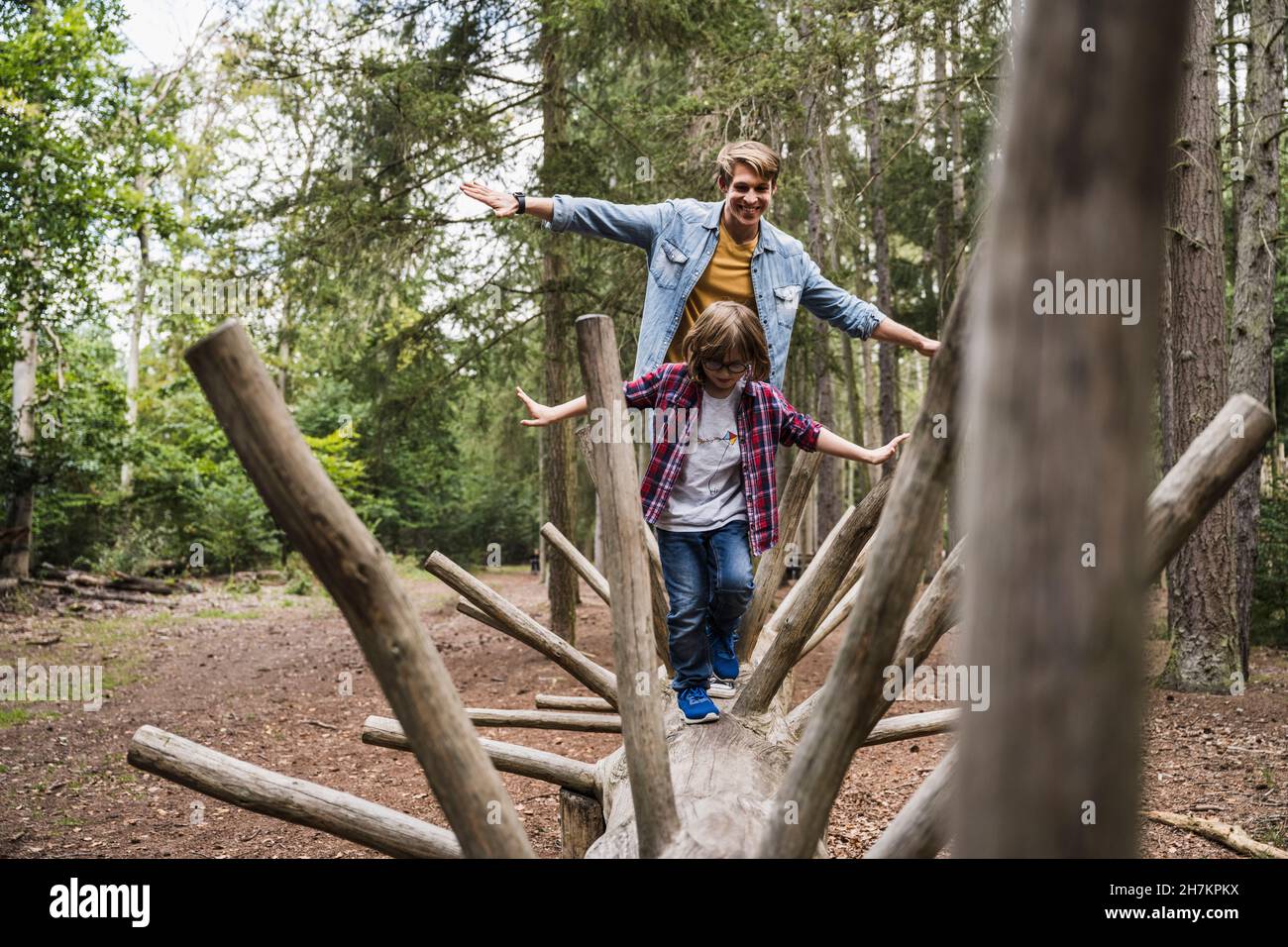 Vater und Sohn mit ausgestreckten Armen gehen auf Baumstamm Stockfoto