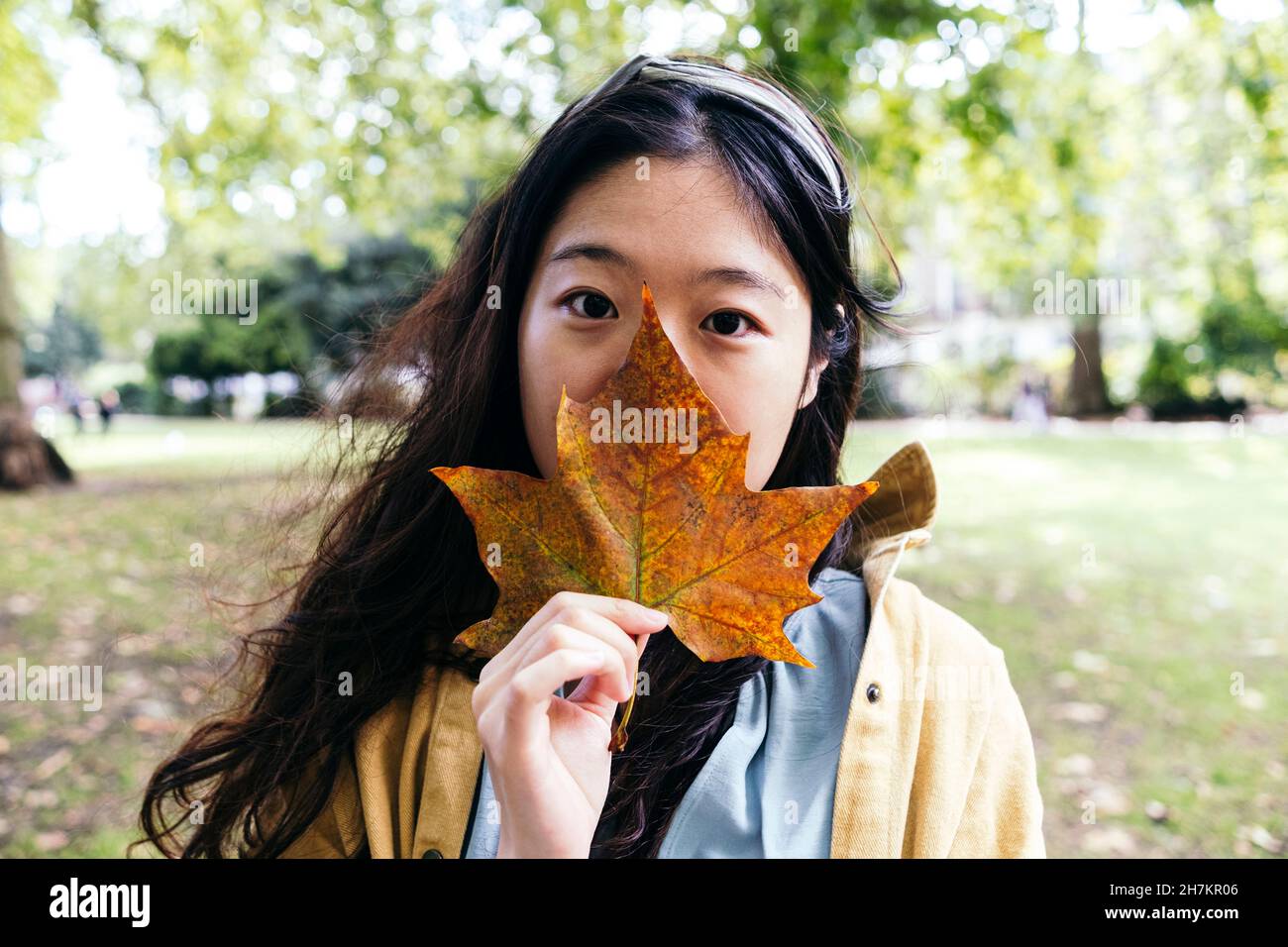 Frau, die im Park den Mund mit Ahornblatt bedeckt Stockfoto