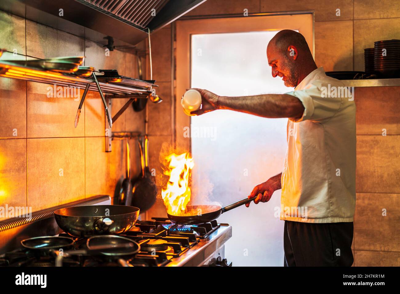 Männlicher Koch mit brennender Flamme, die Öl in die Pfanne gießt Stockfoto