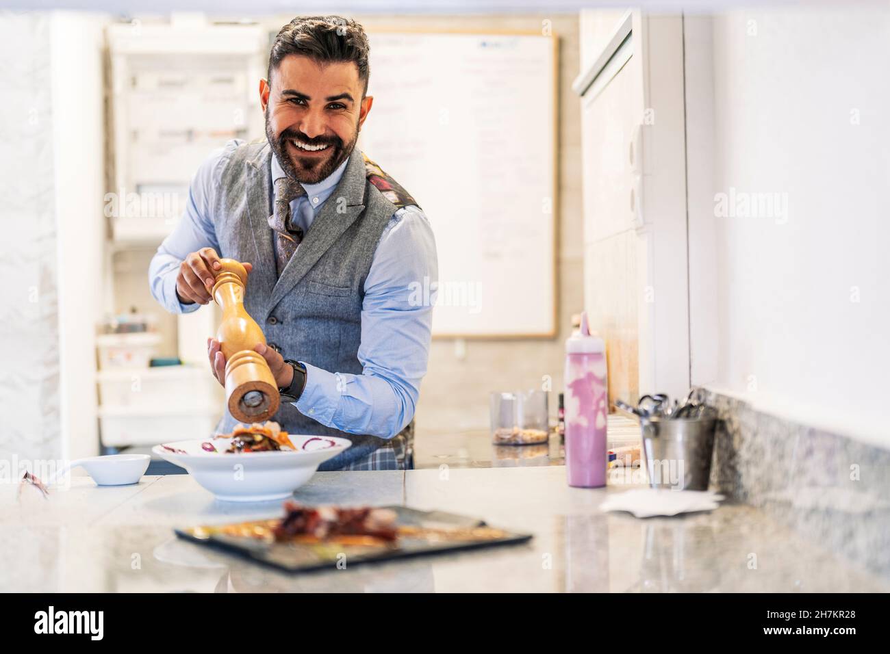 Lächelnder Chefkoch mit Pfeffermühle an der Küchentheke Stockfoto