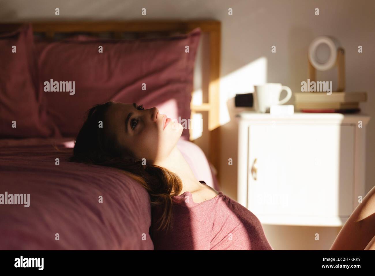Junge Frau in Depressionen, die im Schlafzimmer auf dem Bett gelehnt ist Stockfoto