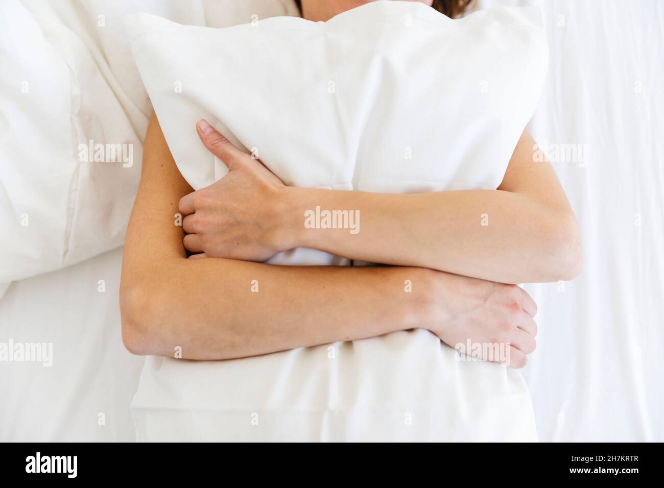 Frau umarmt weißes Kissen, während sie im Schlafzimmer auf dem Bett liegt Stockfoto