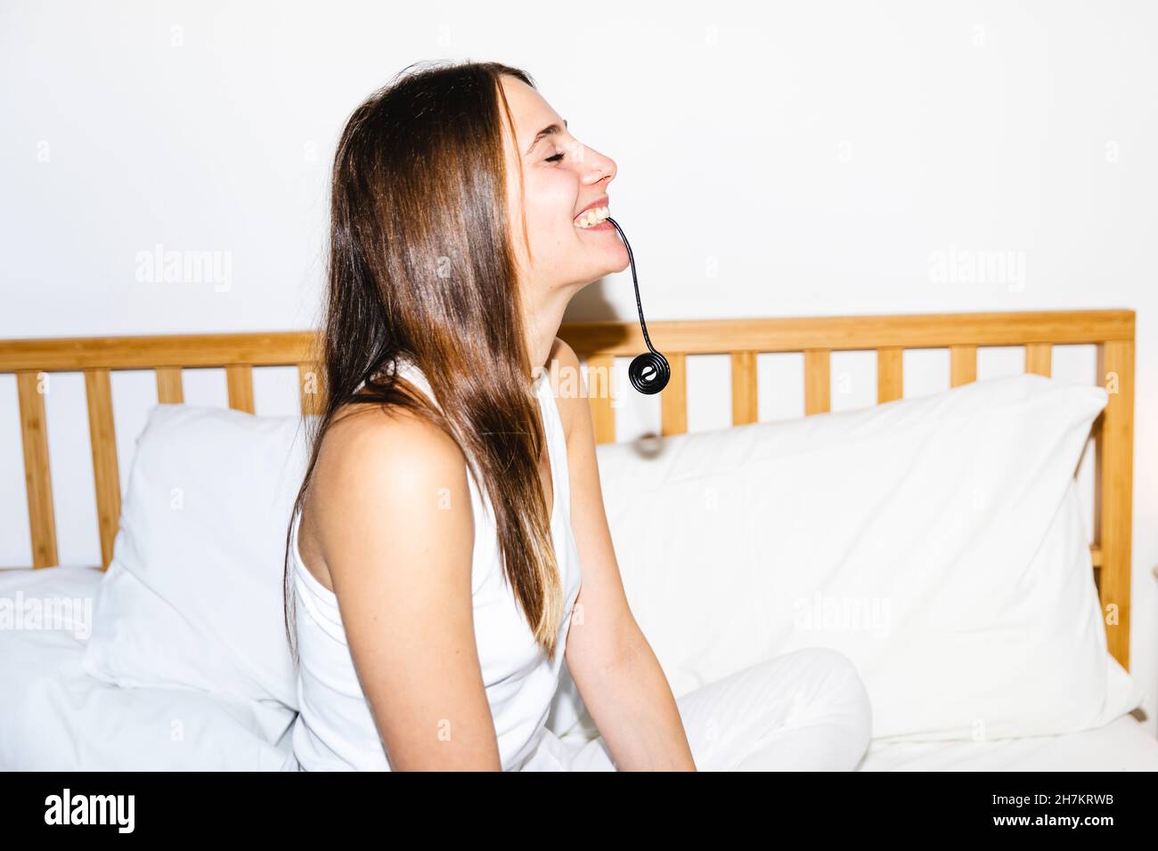 Glückliche junge Frau, die Süßholzbonbons im Schlafzimmer isst Stockfoto