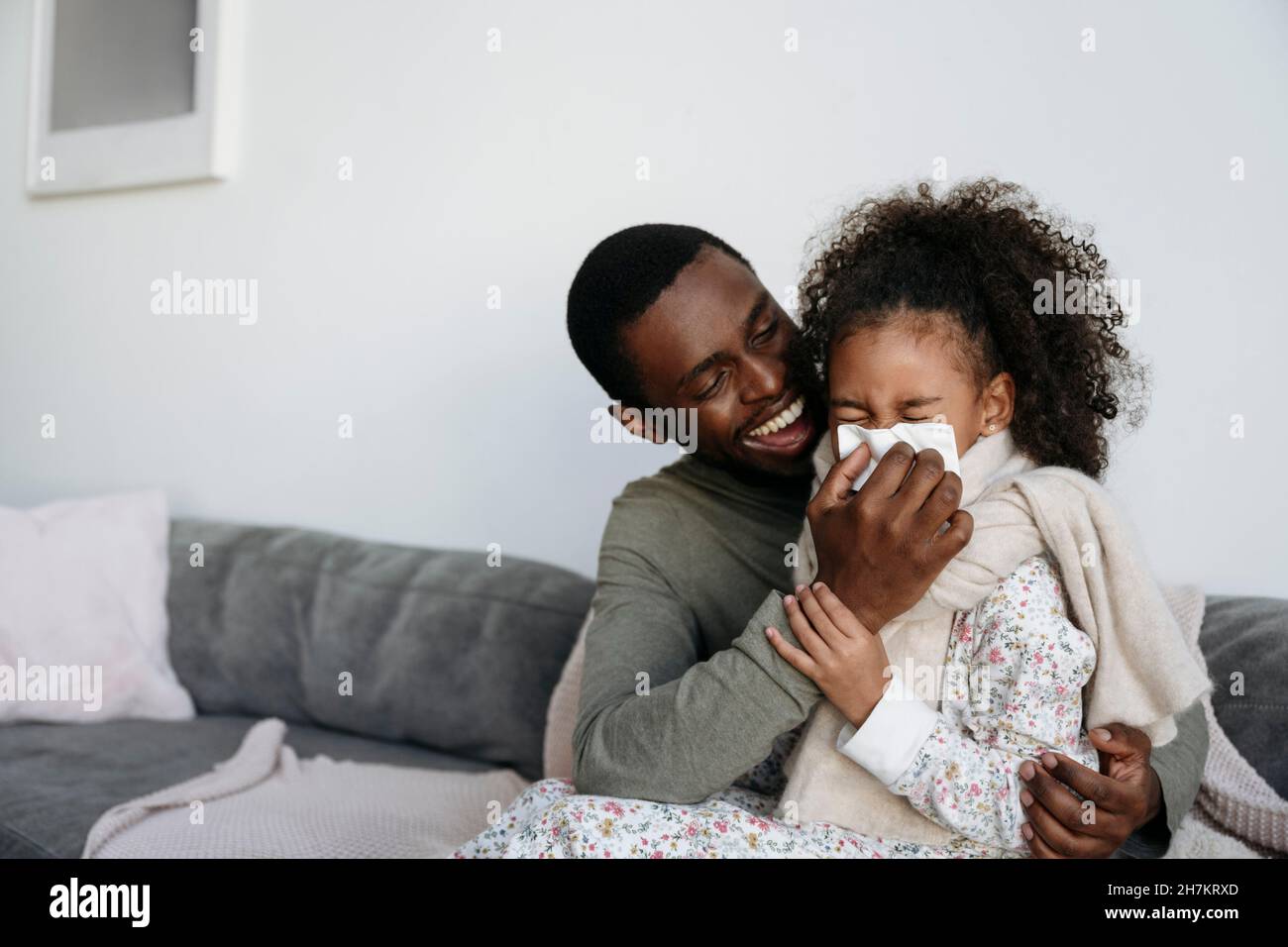 Glücklicher Vater mit Gewebe, das die Nase der Tochter zu Hause abwischt Stockfoto