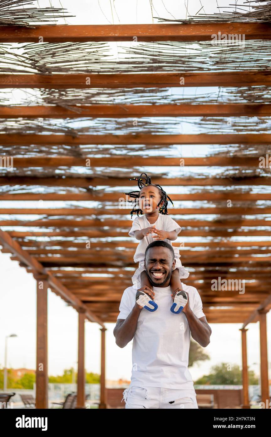 Lächelnder Mann, der Gesicht macht, während er die Tochter auf den Schultern unter dem Dach trägt Stockfoto