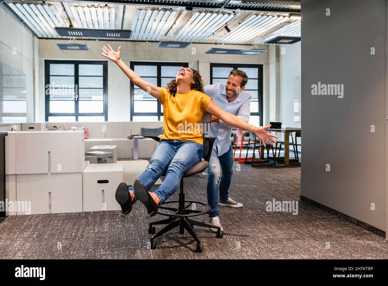 Geschäftsmann schiebt fröhlichen Kollegen auf dem Stuhl im Büro Stockfoto