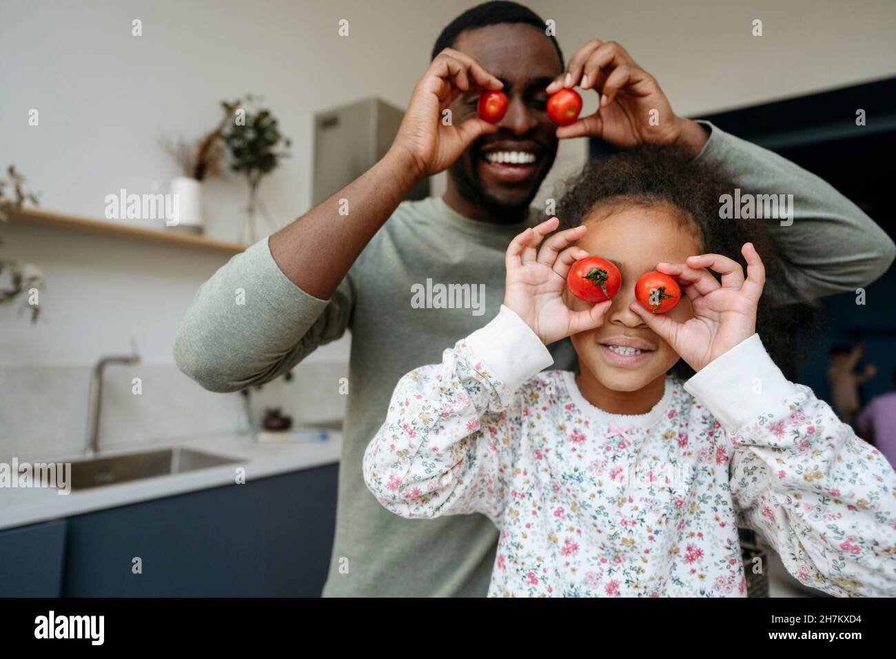 Schelmische Mädchen und Vater spielen mit Tomaten in der Küche Stockfoto