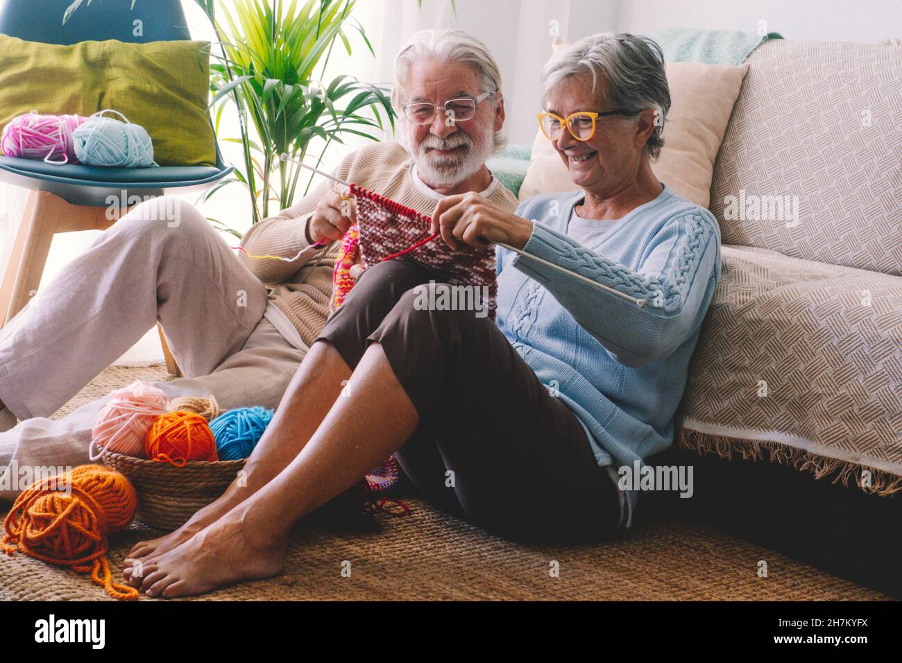 Lächelndes Seniorenpaar strickt Wolle im Wohnzimmer zusammen Stockfoto