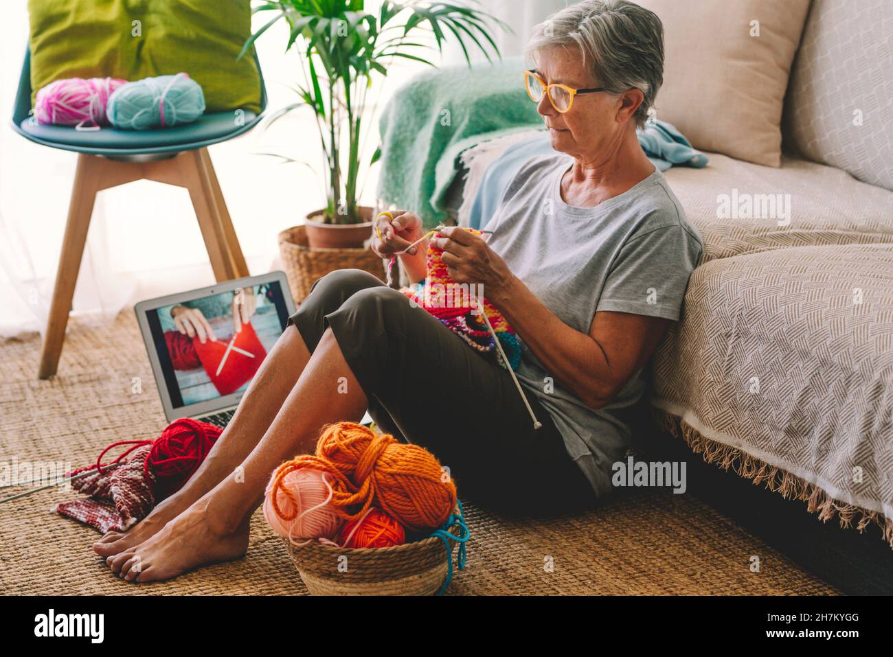 Ältere Frau mit Laptop-Strickwolle im Wohnzimmer Stockfoto