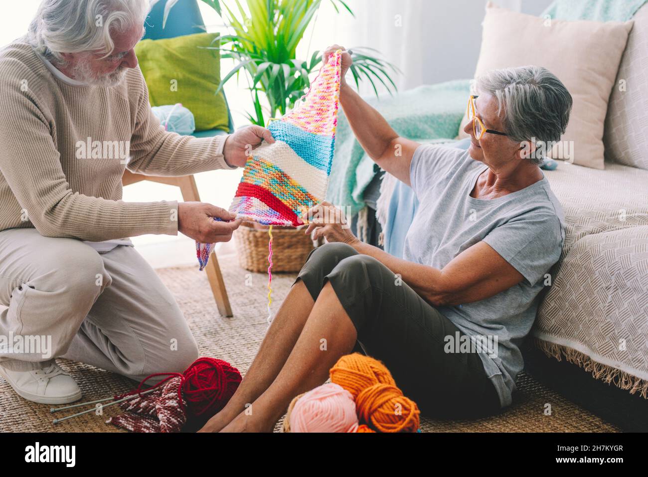 Ältere Frau zeigt dem Mann im Wohnzimmer Strickwolle Stockfoto