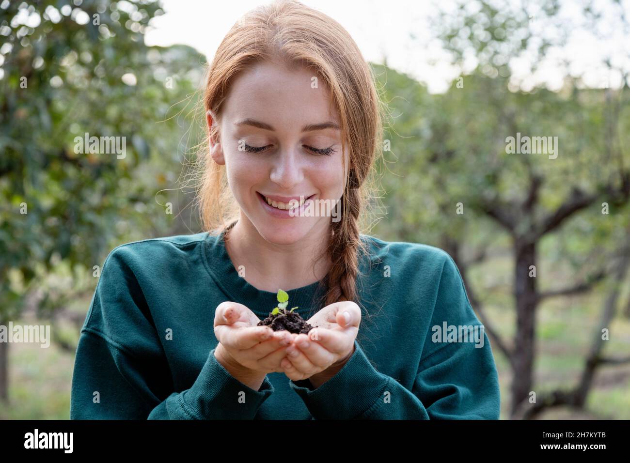 Schöne weibliche Farmerin mit Händen geschmpft halten Pflanze im Garten Stockfoto