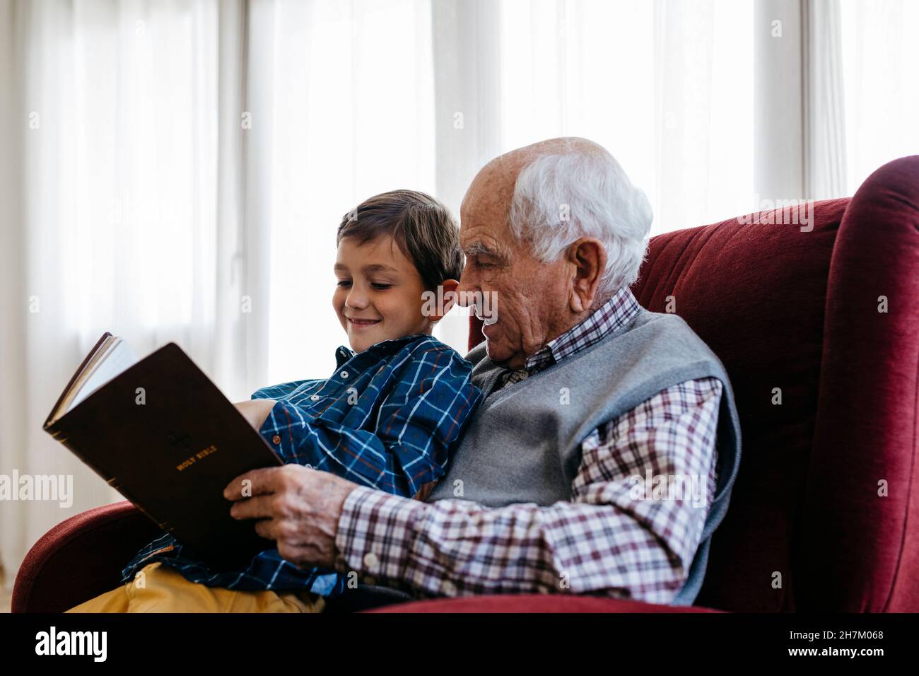 Älterer Mann, der zu Hause ein religiöses Buch liest Stockfoto