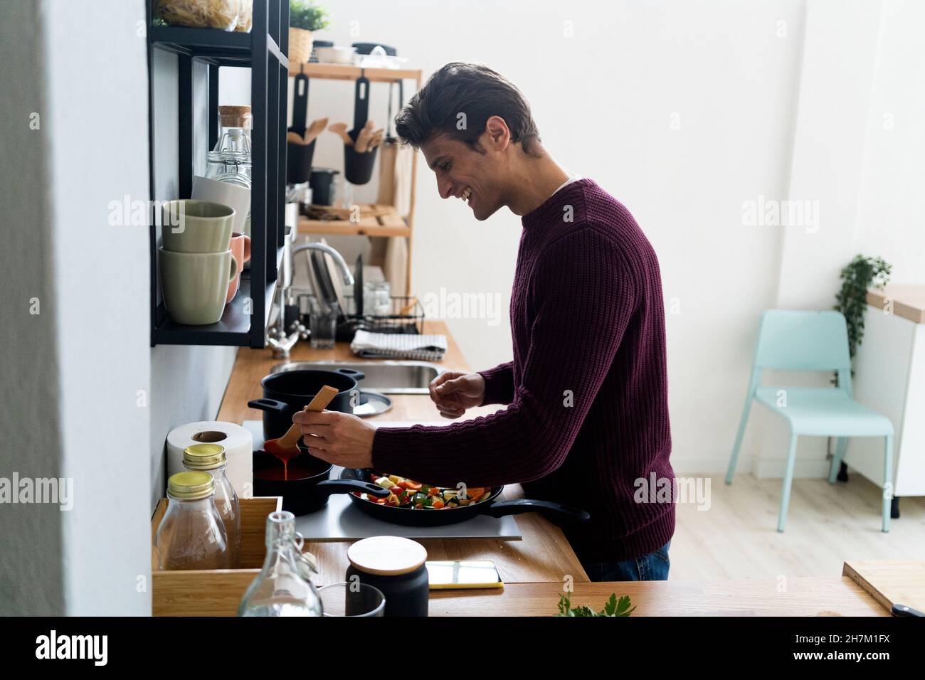 Junger Mann, der zu Hause in der Küche Essen zubereitet Stockfoto