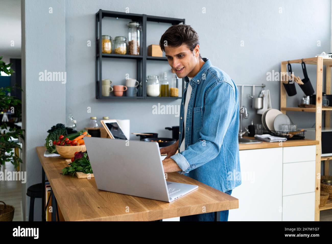 Junger Mann mit digitalem Tablet, während er in der Küche Lebensmittel zubereitete Stockfoto