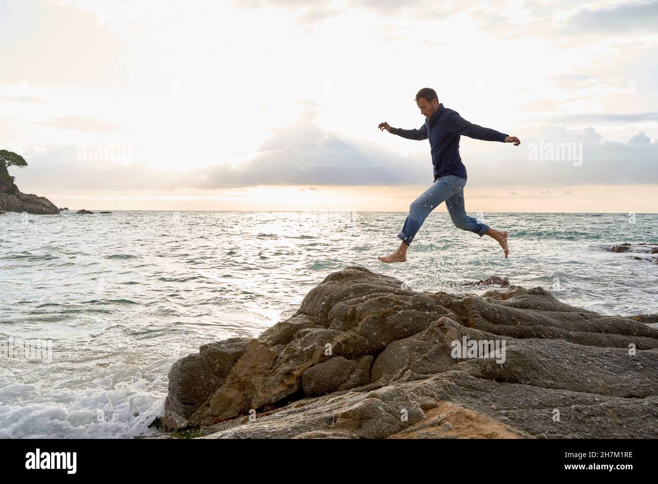 Verspielter Mann, der am Strand über Felsen am Meer springt Stockfoto
