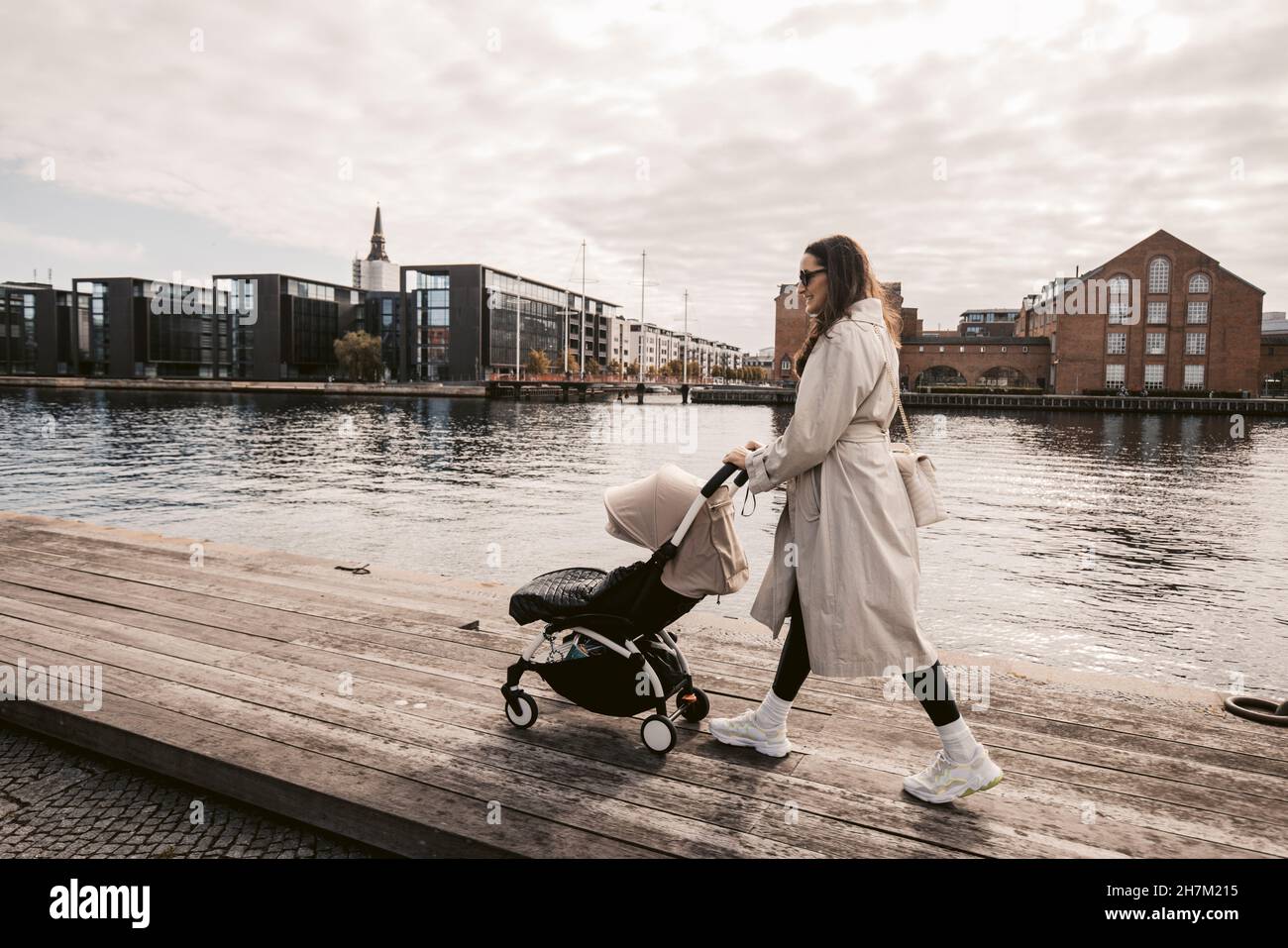 Frau, die mit dem Kinderwagen auf dem Pier am Kanal in Kopenhagen, Dänemark, läuft Stockfoto