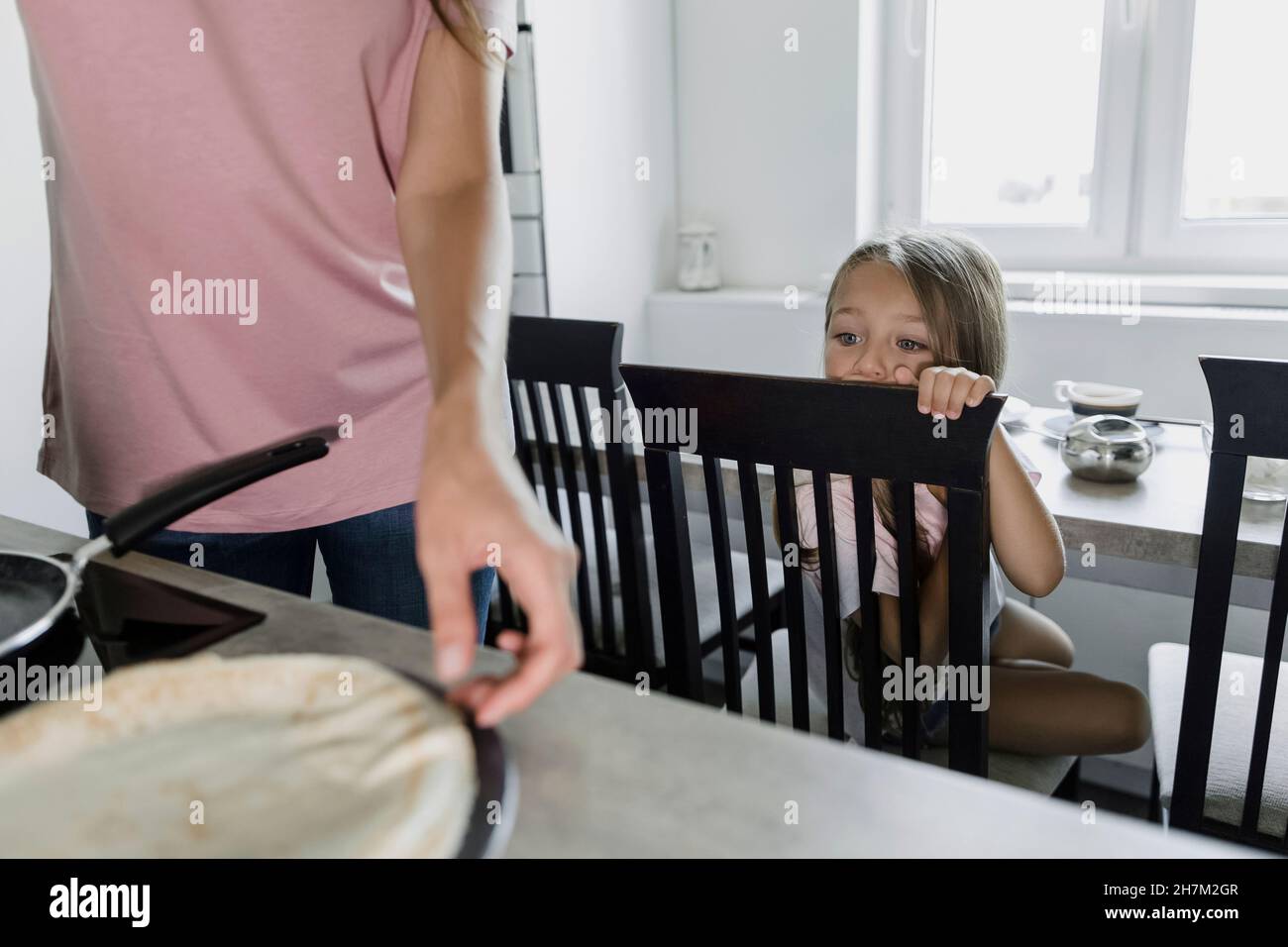 Mädchen, die Mutter beim Kochen von Pfannkuchen in der Küche ansieht Stockfoto