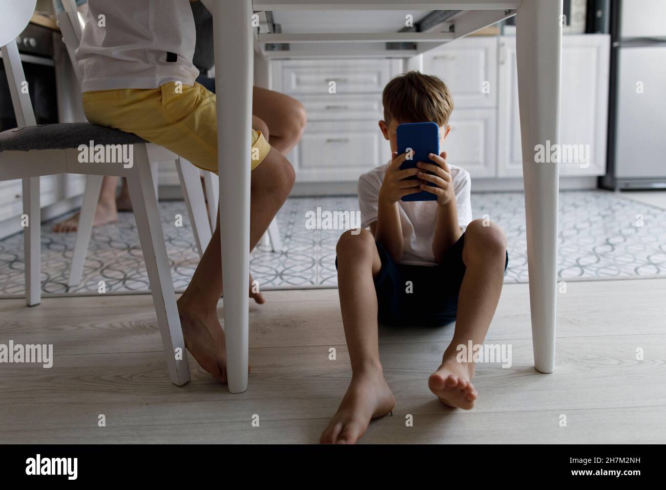 Junge, der zu Hause unter dem Tisch ein Mobiltelefon benutzt Stockfoto