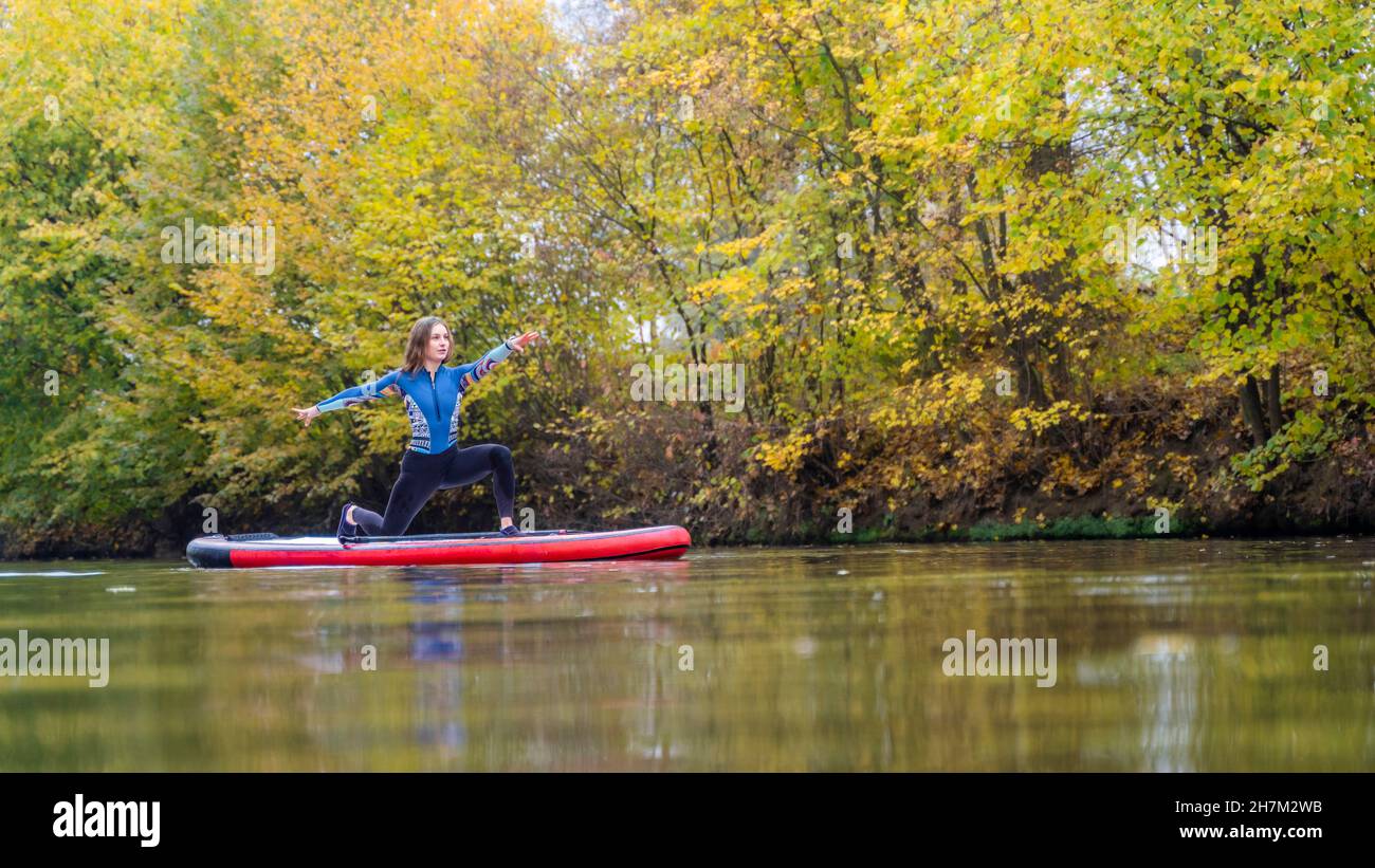 Junge Sportlerin, die Yoga praktiziert, posiert auf dem Paddleboard am Rems Fluss, Baden-Württemberg, Deutschland Stockfoto