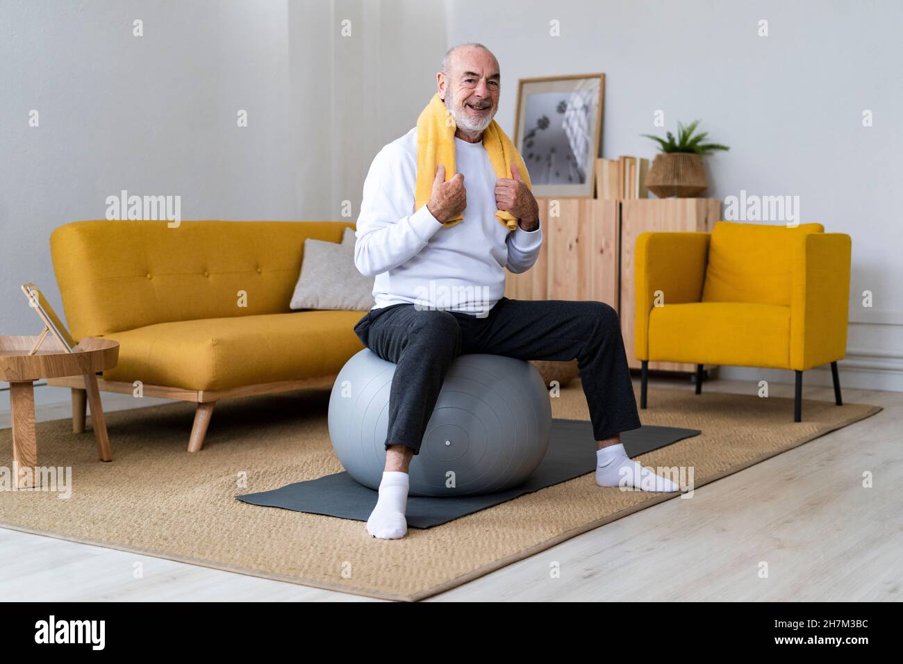 Lächelnder älterer Mann, der zu Hause eine Wasserflasche auf dem Fitnessball hält Stockfoto