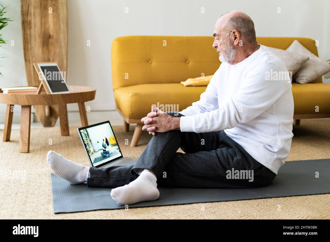 Glücklicher älterer Mann mit Mobiltelefon, der zu Hause auf dem Fitnessball sitzt Stockfoto