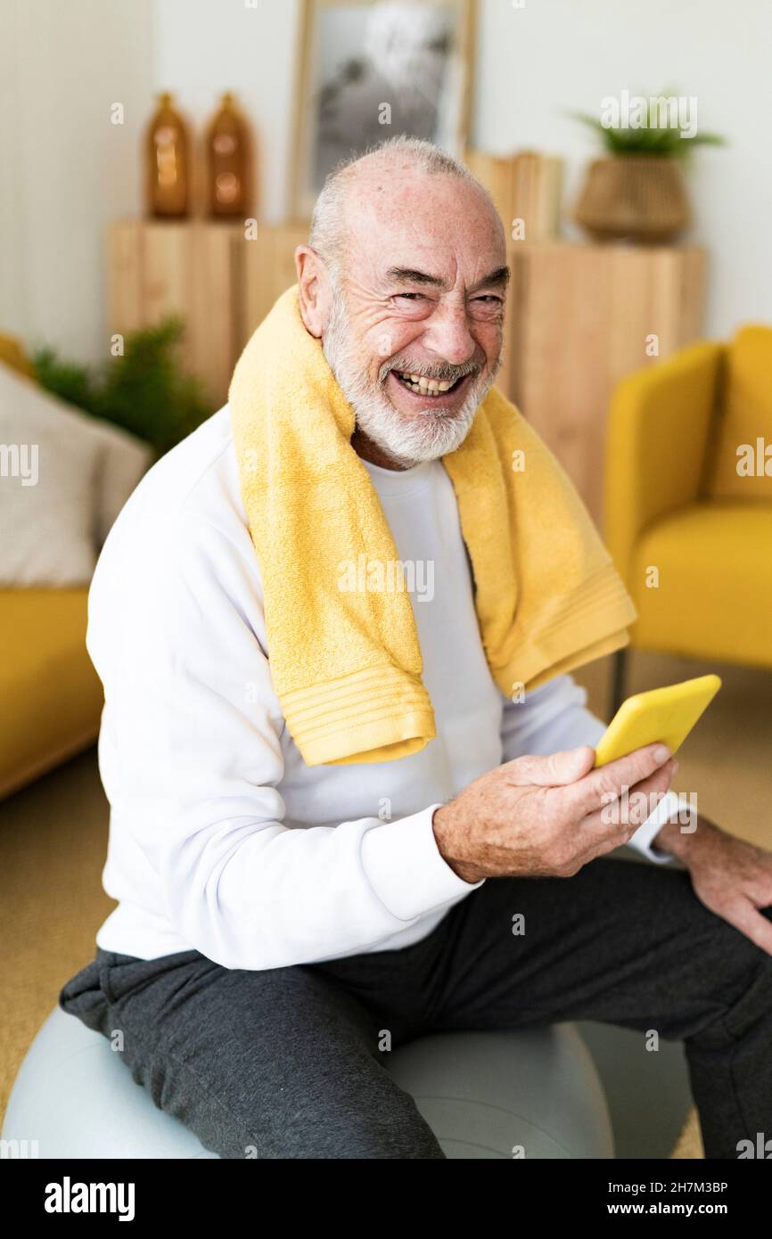 Mann mit Smartphone auf Fitness-Ball im Wohnzimmer Stockfoto