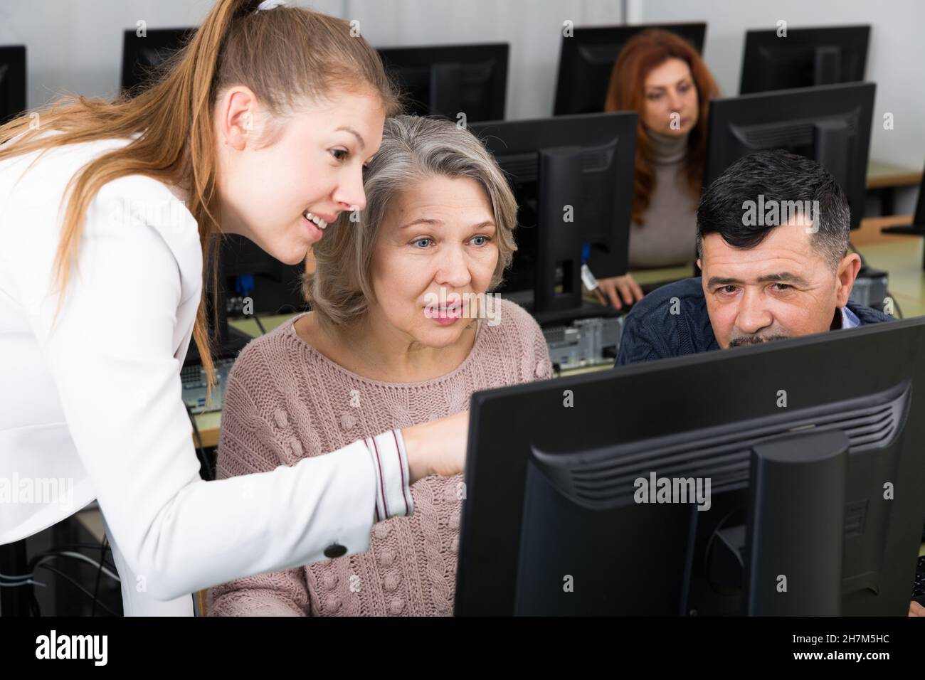 Junge Lehrerin hilft reifen Menschen, Computer zu benutzen Stockfoto