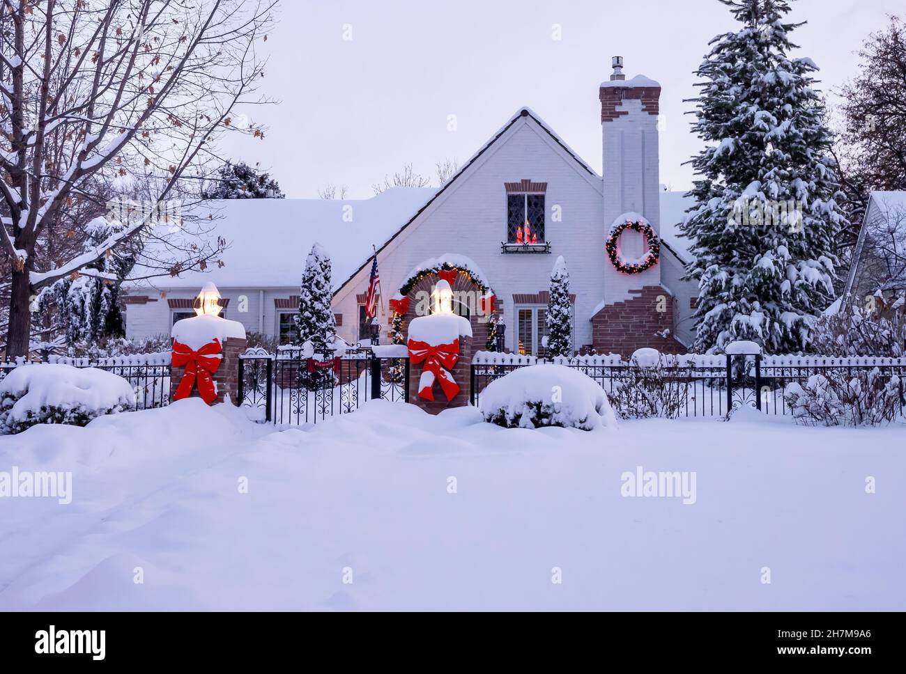 Ein festliches, einladendes Haus, schön dekoriert mit Bändern, einem Kranz und glühenden Kerzen, bedeckt mit Schnee und bereit für Feiertage. Stockfoto Ein festliches, einladendes Haus, schön dekoriert mit Bändern, einem Kranz und glühenden Kerzen, bedeckt mit Schnee und bereit für Feiertage. Stockfoto