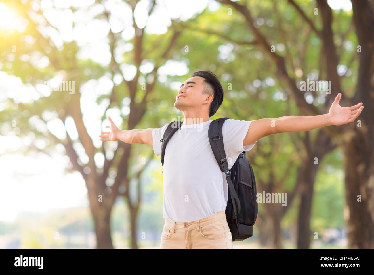 Entspannter junger Mann, der tief frische Luft in einem Wald mit grünen Bäumen atmet Stockfoto