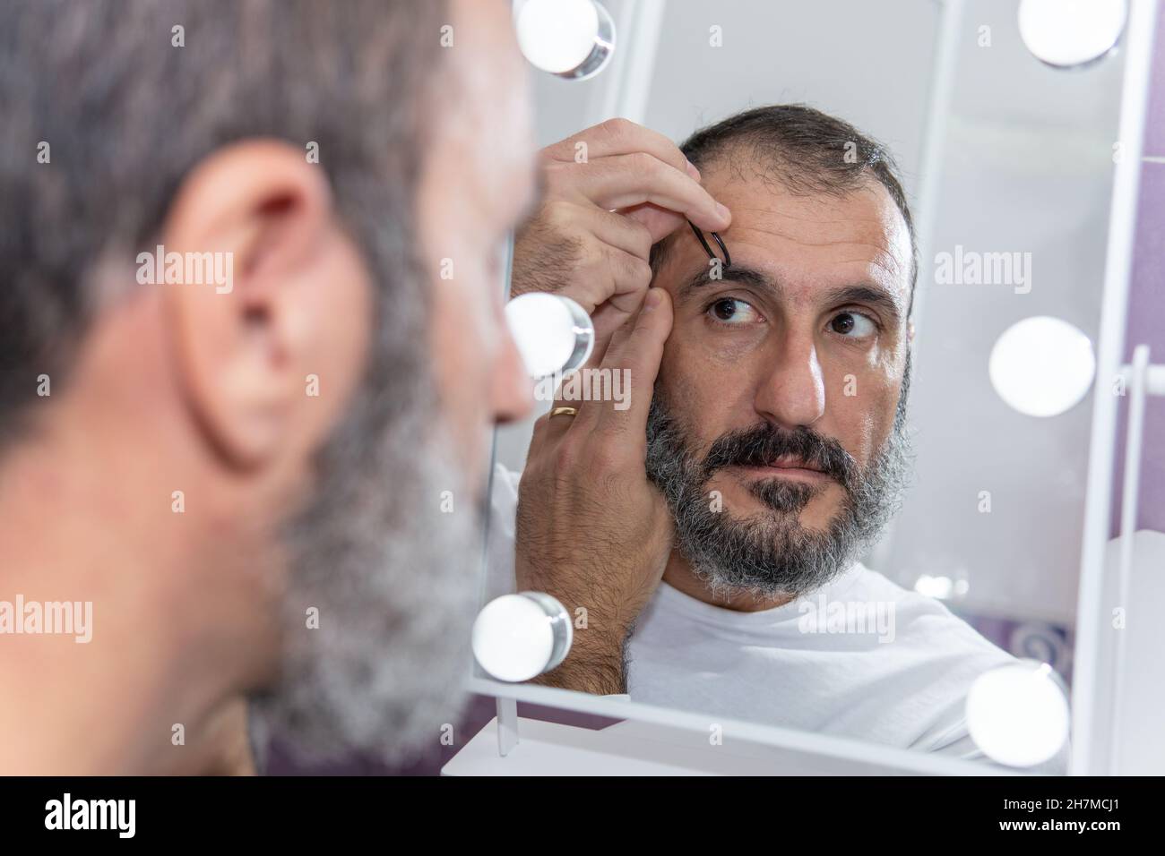Kaukasischer reifer Mann, der seine Augenbrauen mit einer Pinzette in Fron zupft Stockfoto