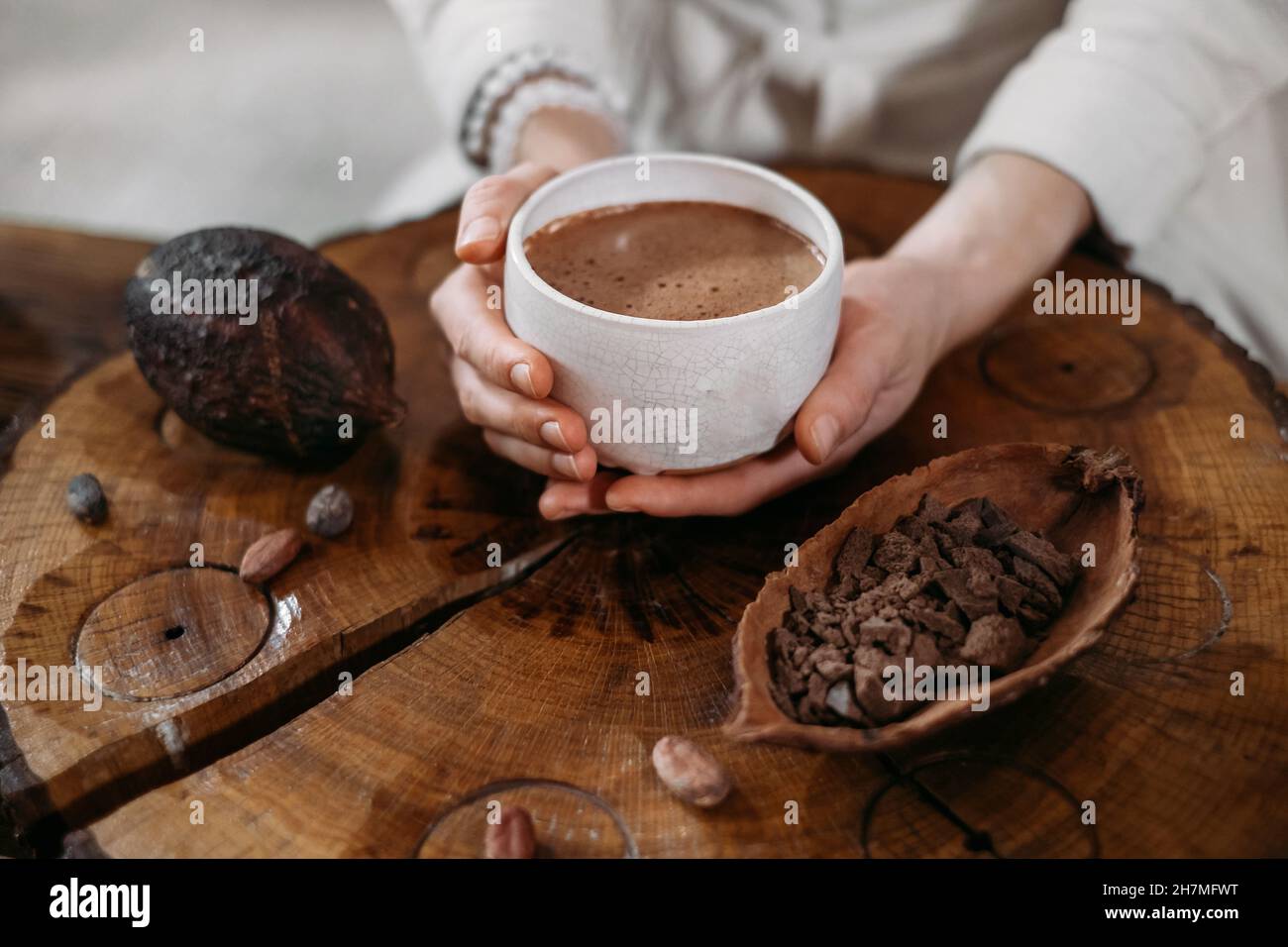 Heißer handgemachter zeremonieller Kakao in weißer Tasse. Frau Hände halten Handwerk Kakao, Draufsicht auf Holztisch. Bio gesundes Schokoladengetränk aus zubereitet Stockfoto