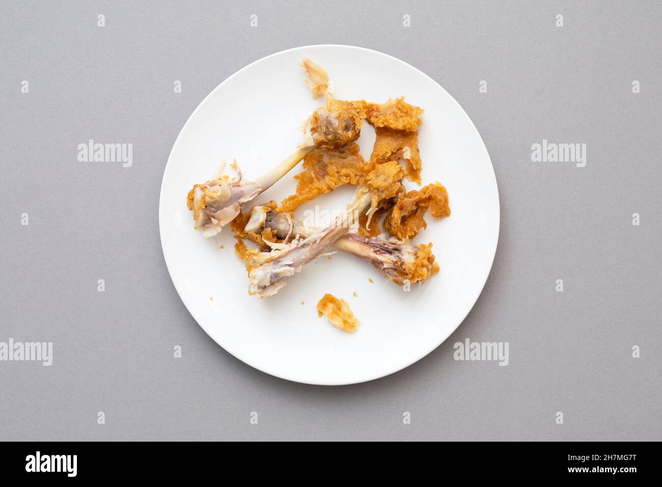 Chaotische Essensreste, Hühnerknochen als Fast Food auf der weißen Keramikplatte, Draufsicht Stockfoto
