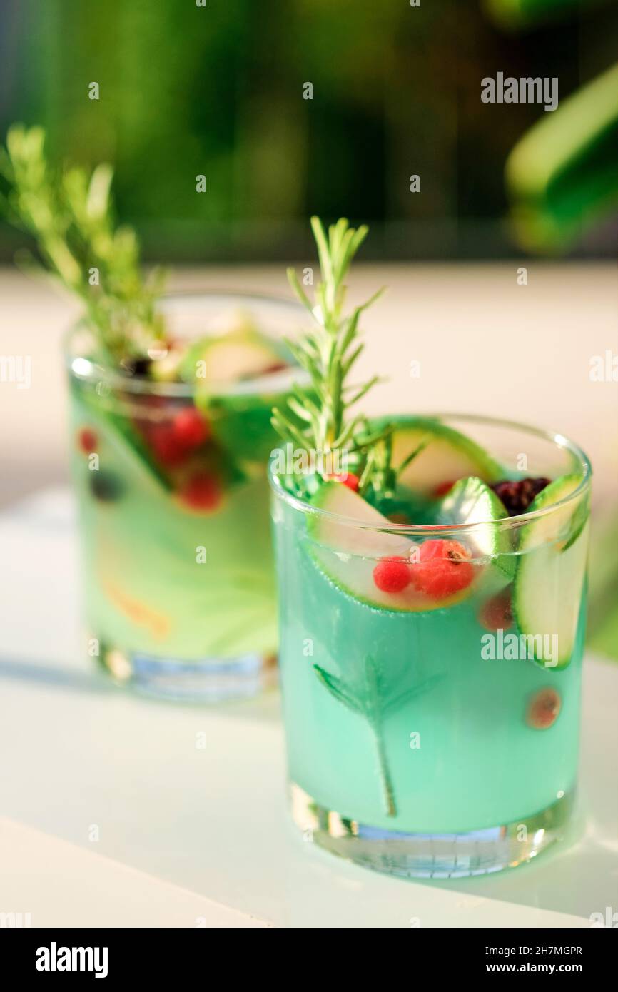 Zwei Gläser mit grüner Limonade aus Zitronensmarin und Minze in Gläsern auf dem Tisch auf der Terrasse. Kaltes, erfrischendes Getränk für den heißen Sommertag. Grüne Monstera Blätter auf dem Hintergrund. Stockfoto