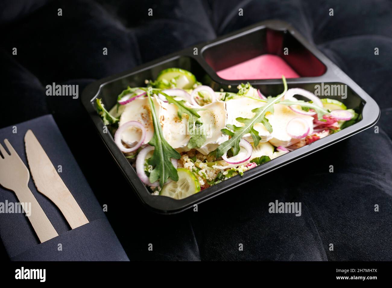 Grüner Salat zum Mitnehmen mit Camembert-Käse appetitliches Fertiggericht in einer Einwegbox. Kulinarische Fotografie. Hintergrund der Speisen. Stockfoto