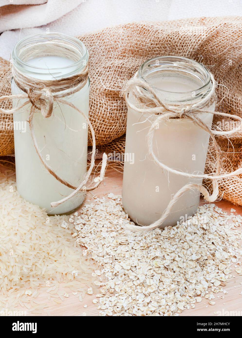 Reismilch mit losen Reiskörnern und Hafermilch mit rohem Hafer auf einem rustikalen Tischgestelle mit Kopierfläche Stockfoto