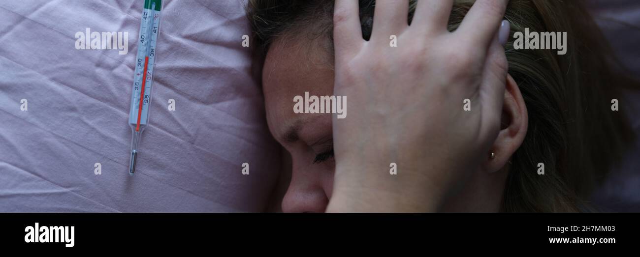 Junge Frau im Bett und hielt ihren Kopf in der Nähe des Quecksilberthermometers Stockfoto